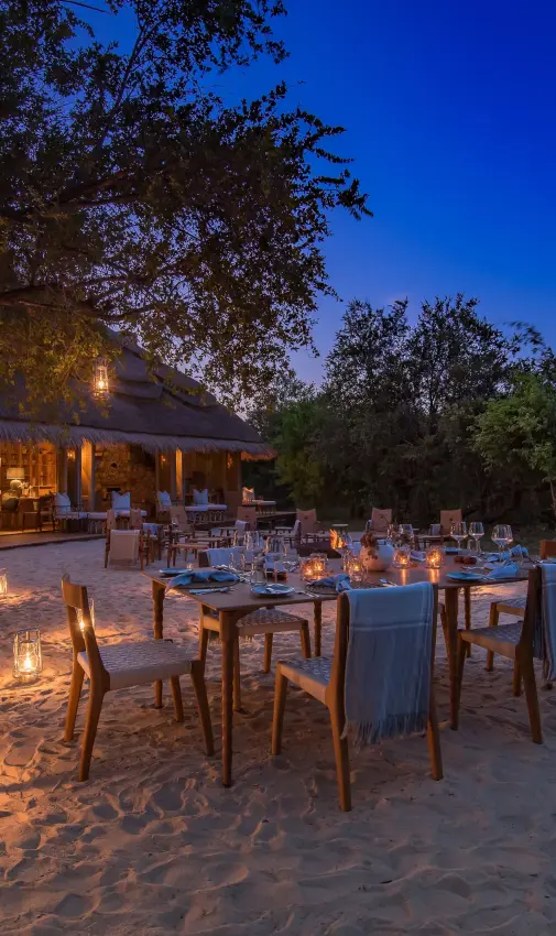 Outdoor dining setup on sand at dusk with lanterns, Mpala Jena, Victoria Falls, Zimbabwe