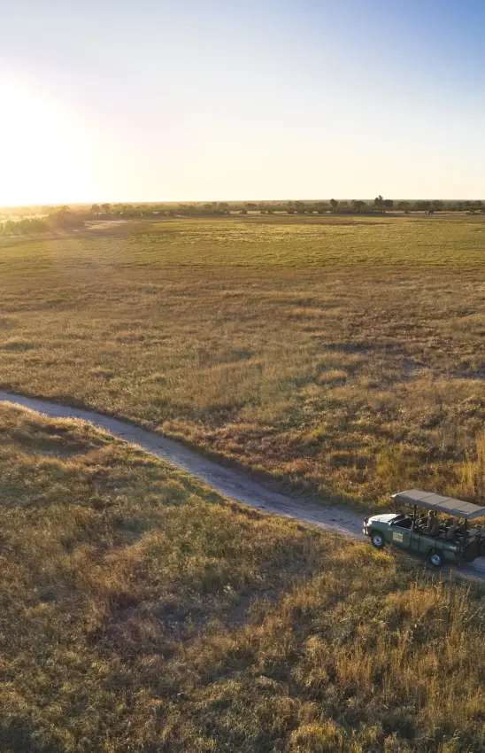 Open-air safari vehicle on game drive crossing shallow river through grassland, Muddy Teak, Hwange National Park, Zimbabwe