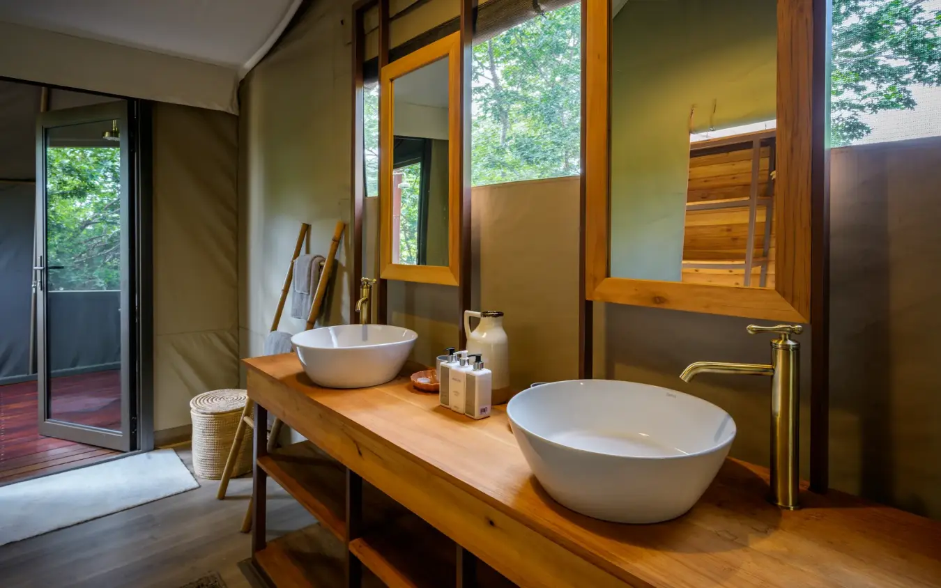 Luxury bathroom with dual vessel sinks and forest views through large windows, Muddy Teak, Hwange National Park, Zimbabwe