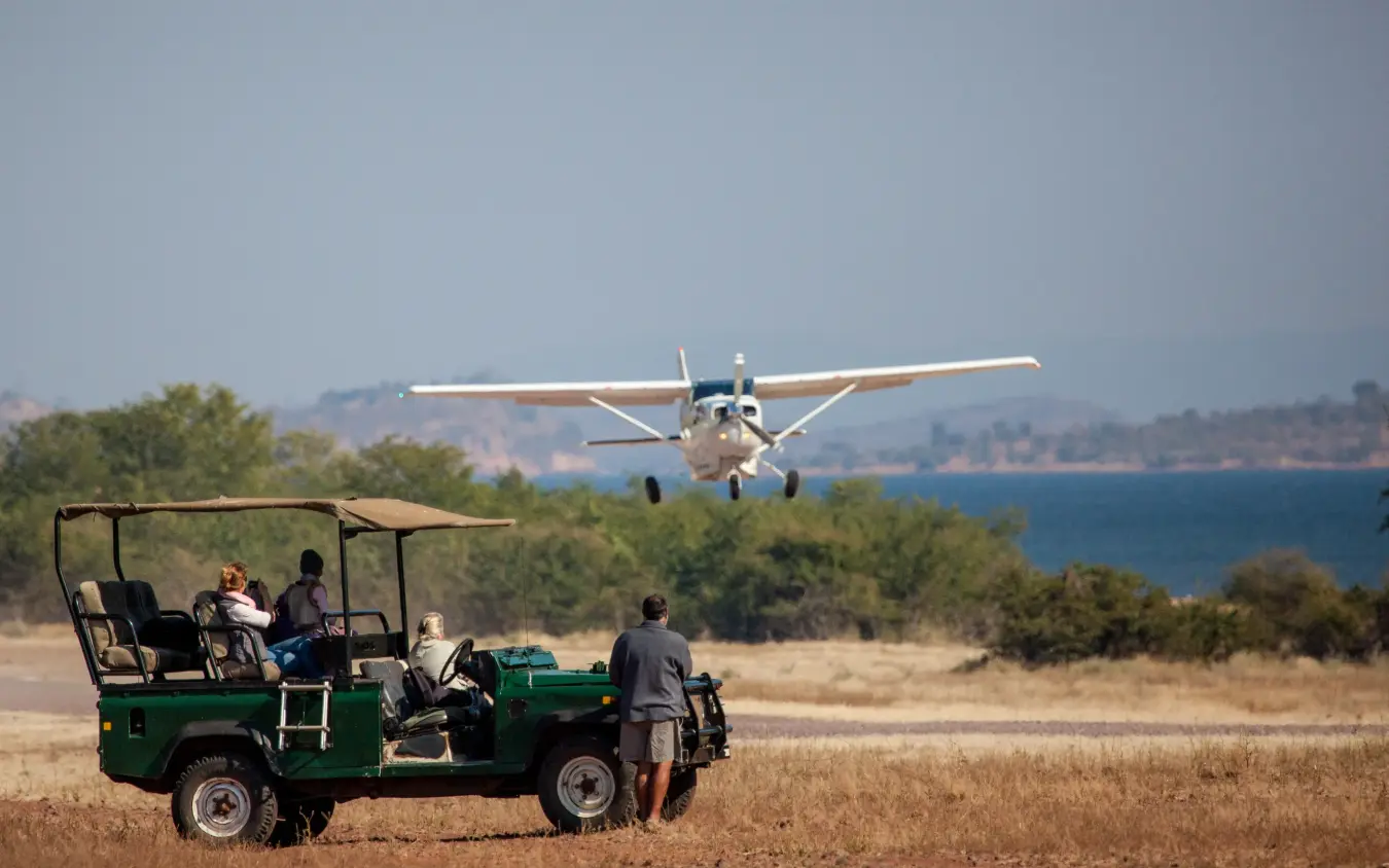 Small aircraft landing near safari vehicle with guests watching, Matusadona, Zimbabwe