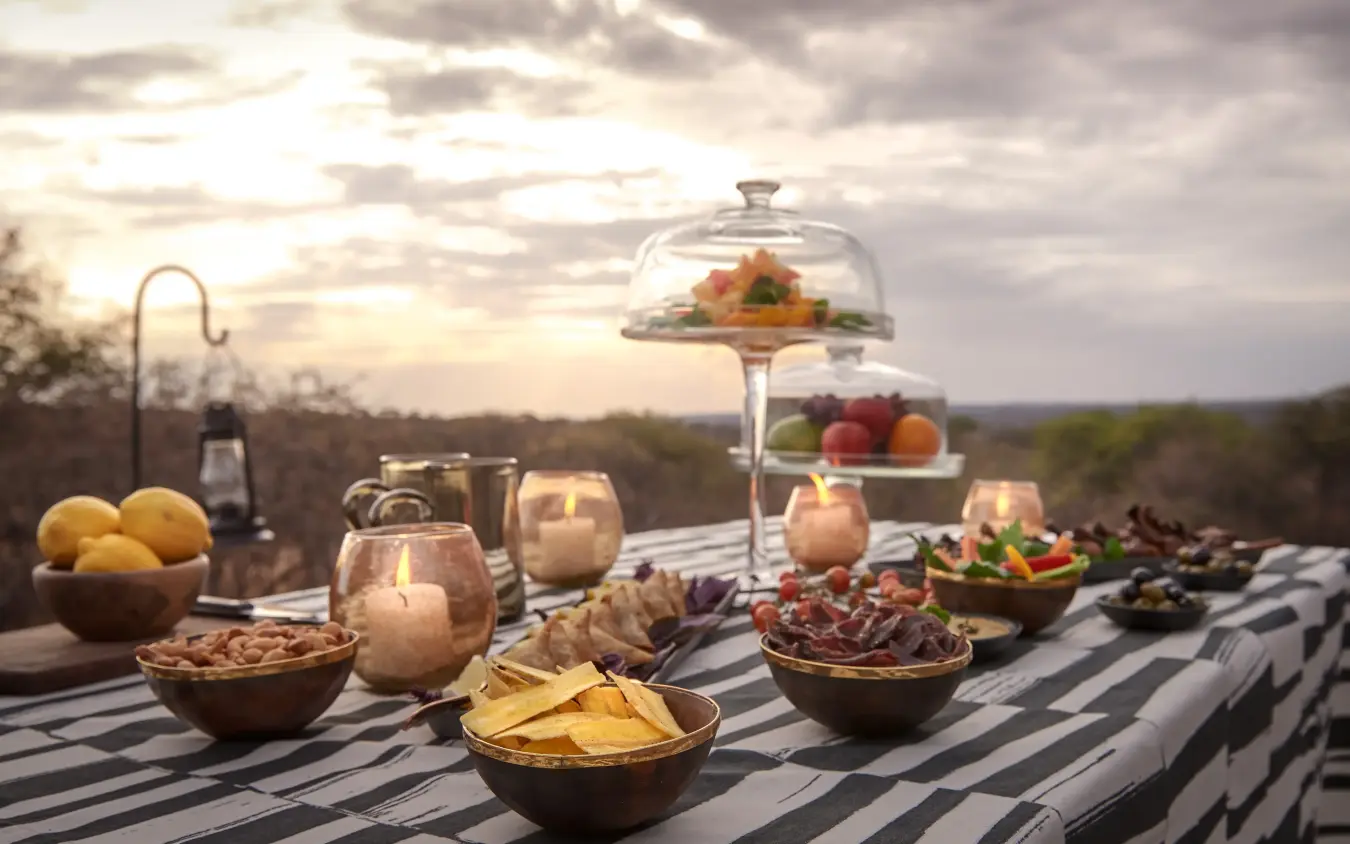 Outdoor dining setup with food and savanna landscape backdrop, Mwiba Lodge, Serengeti National Park, Tanzania