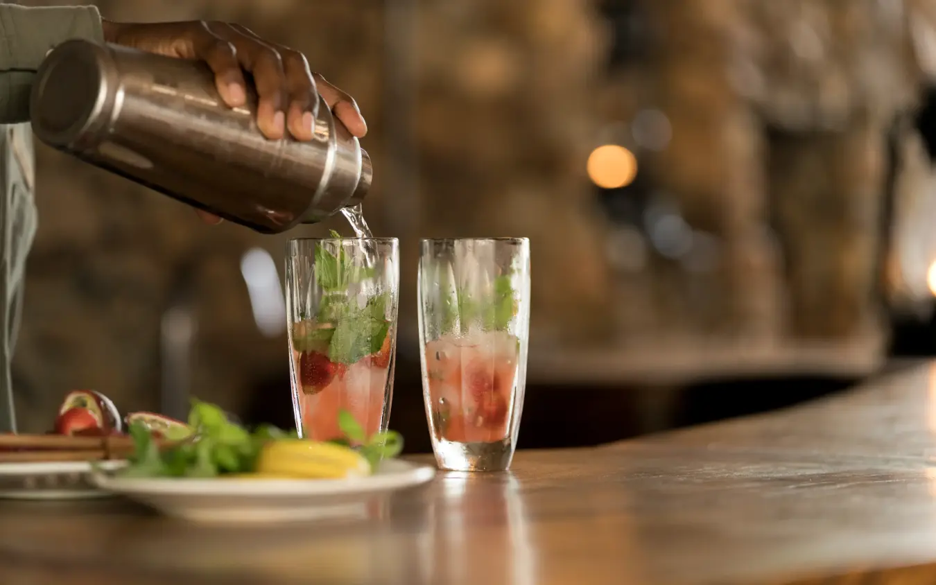 Bartender pouring cocktail into glasses with mint garnish, Mwiba Lodge, Serengeti National Park, Tanzania