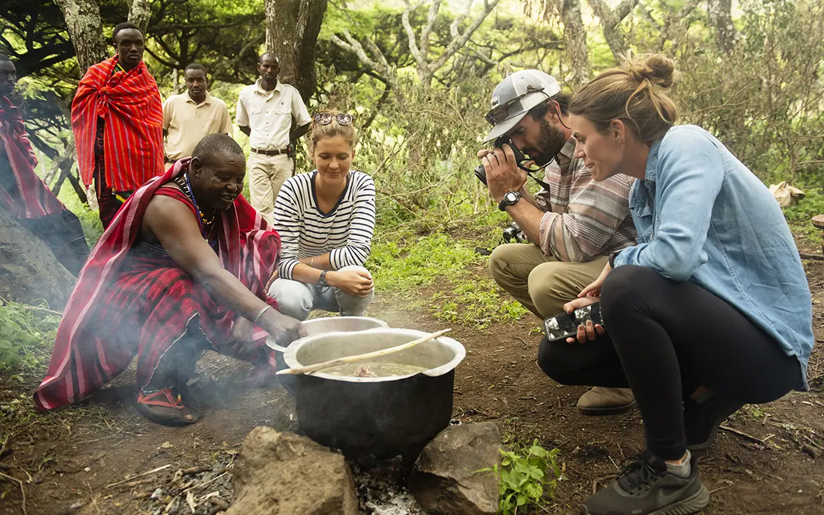 Guests observe traditional cooking preparation in forest setting, Mysigio Camp, Ngorongoro Crater, Tanzania