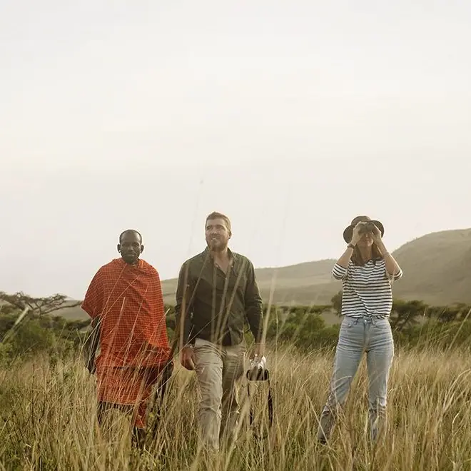 Three people walking through grassland with hills behind, Mysigio Camp, Ngorongoro Crater, Tanzania