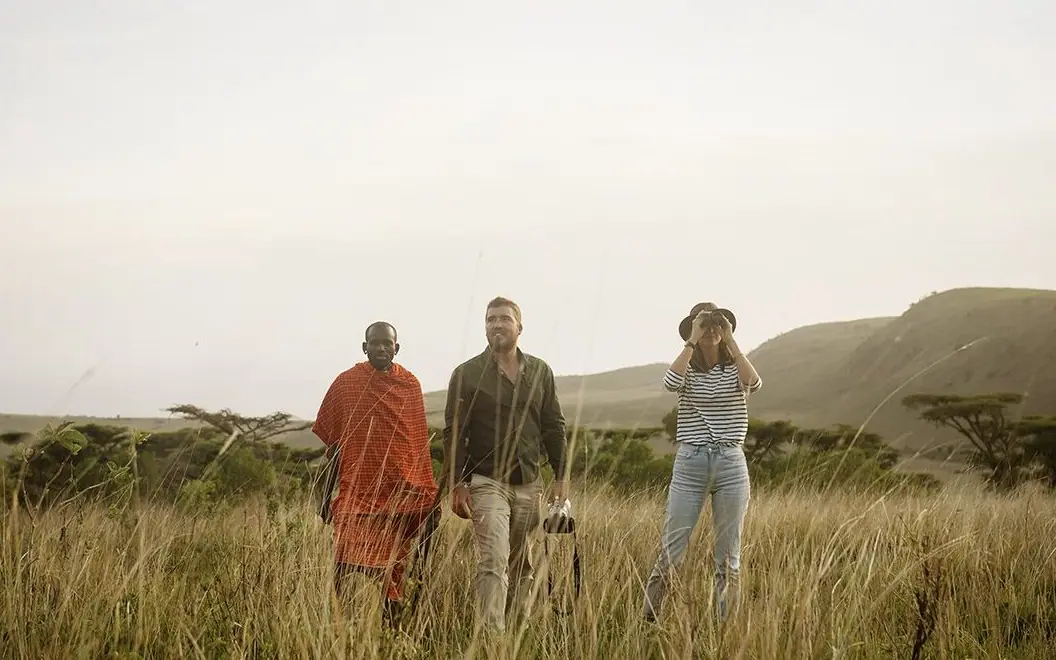 Three people walking through grassland with hills behind, Mysigio Camp, Ngorongoro Crater, Tanzania