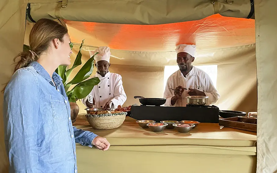 Chef demonstrating cooking techniques to guest at camp kitchen, Mysigio Camp, Ngorongoro Crater, Tanzania