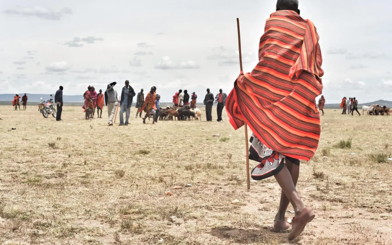 Person in red cloth walking across savanna landscape, Naboisho Camp, Maasai Mara, Kenya