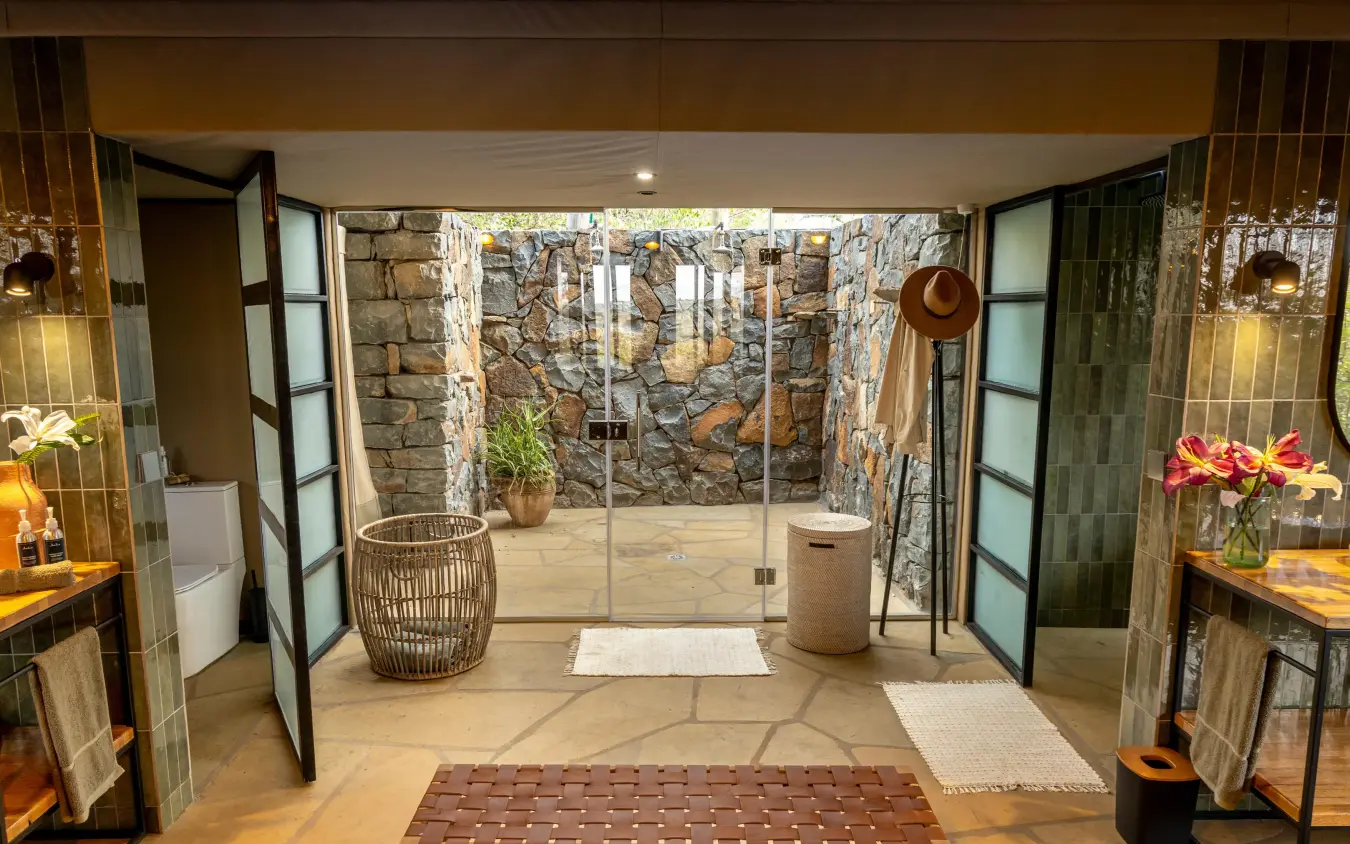 Luxury bathroom with stone walls and glass doors opening to outdoor courtyard, Naboisho Camp, Maasai Mara, Kenya