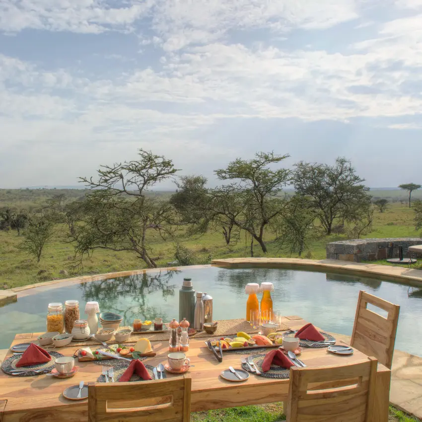 Dining table set overlooking savanna landscape and pool, Naboisho Camp, Maasai Mara, Kenya
