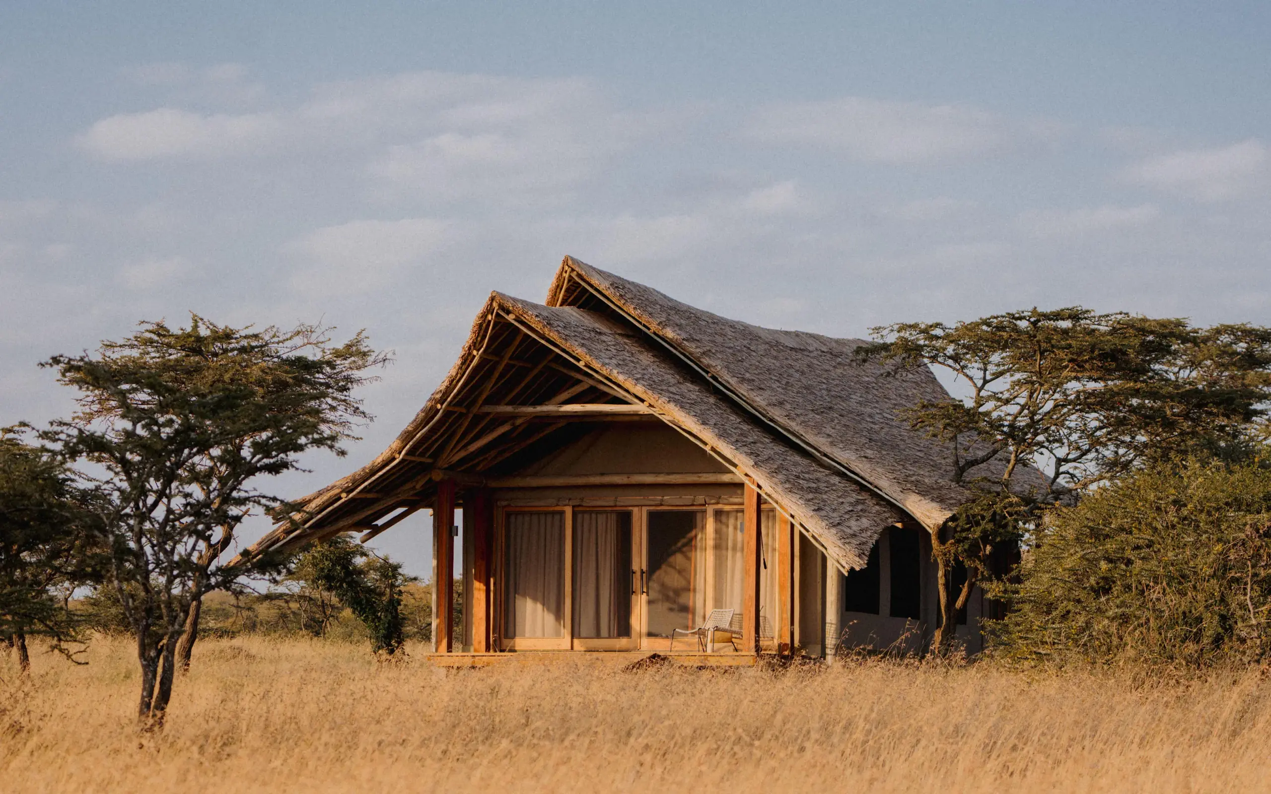 Thatched-roof safari lodge in golden grassland at sunset, Naboisho Camp, Maasai Mara, Kenya