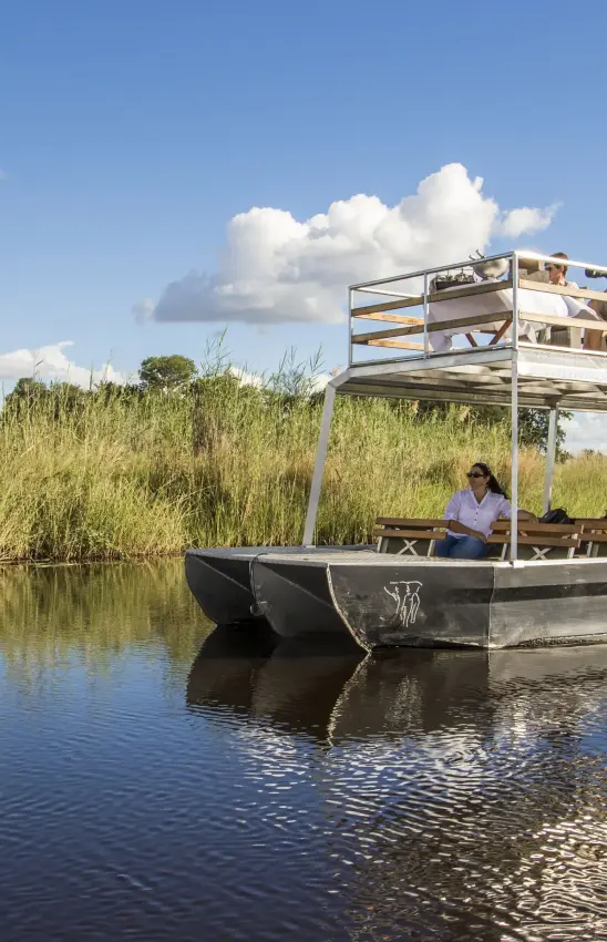 Flat-bottomed boat with canopy on waterway lined with reeds and wetland vegetation, Nambwa Tented Lodge, Zambezi Region, Namibia