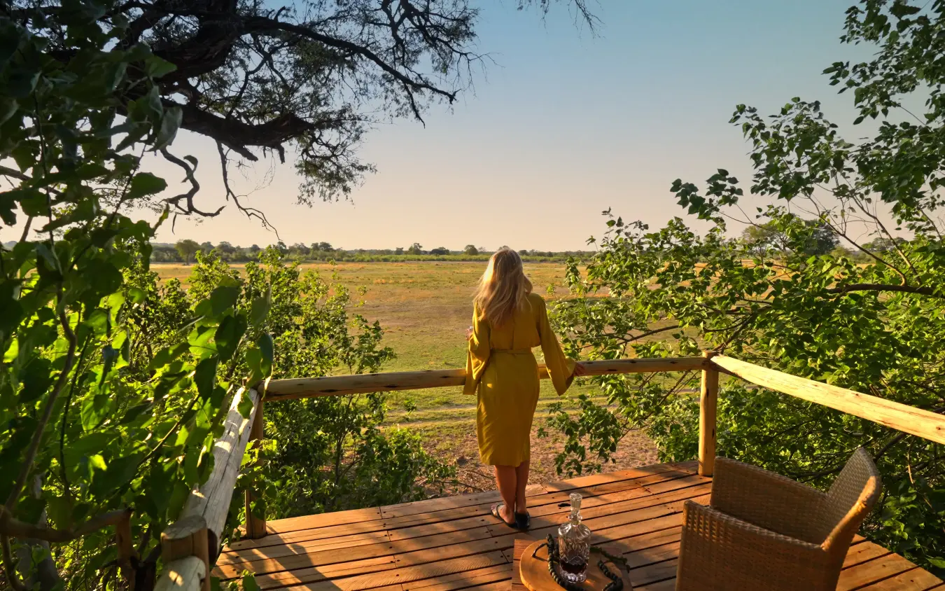 Woman on wooden deck overlooking vast grassland at golden hour, Nambwa Tented Lodge, Zambezi Region, Namibia