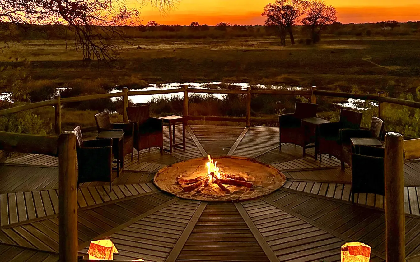 Wooden deck with central fire pit overlooking waterhole at sunset, Nambwa Tented Lodge, Zambezi Region, Namibia