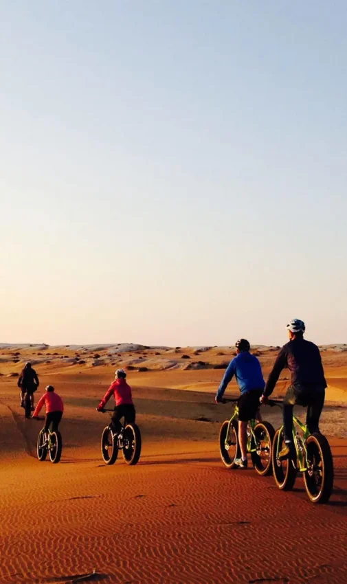 Cyclists riding across red sand dunes at sunset, Swakopmund, Namibia