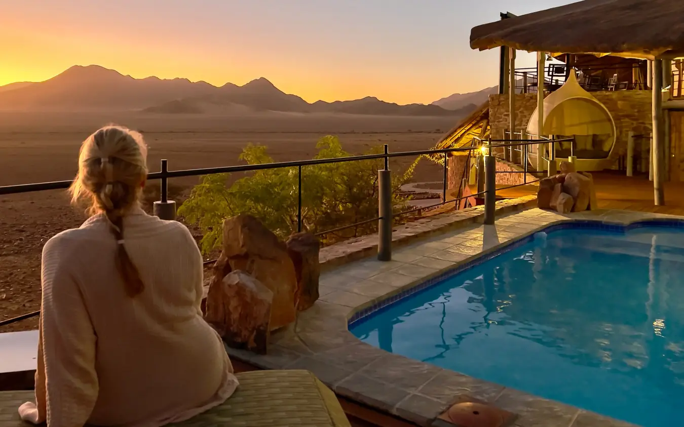 Woman relaxing by pool at sunset overlooking desert mountain landscape, Namib Outpost, Sossusvlei, Namibia