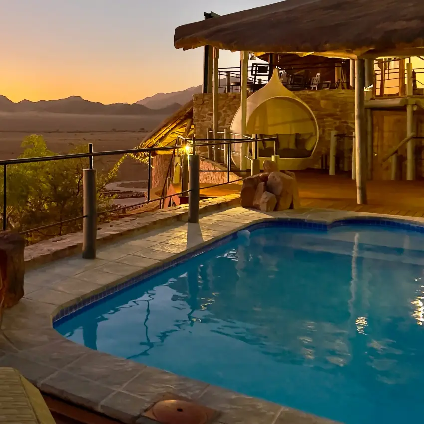 Woman relaxing by pool at sunset overlooking desert mountain landscape, Namib Outpost, Sossusvlei, Namibia