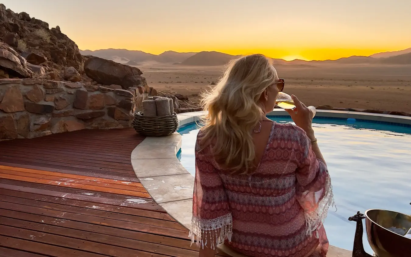 Woman enjoying sunset view from pool deck overlooking desert valley, Namib Outpost, Sossusvlei, Namibia