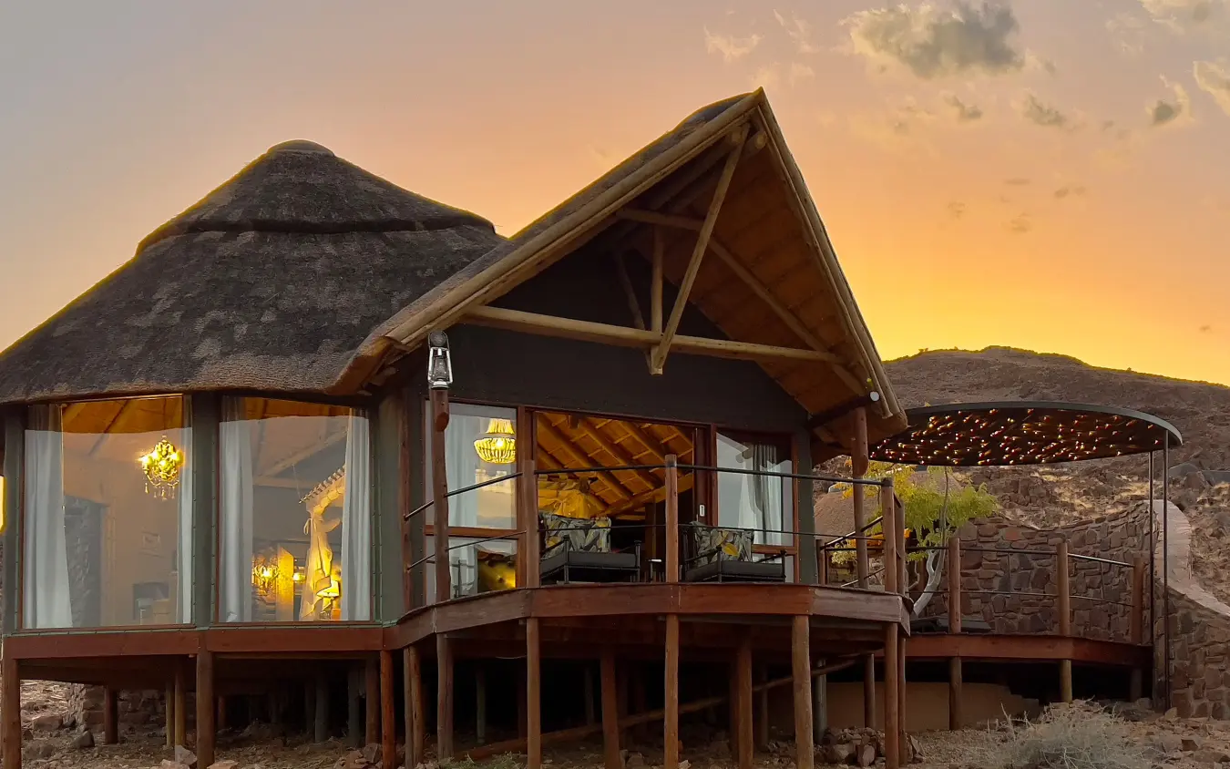 Luxury lodge with thatched rondavel at sunset in arid landscape, Namib Outpost, Sossusvlei, Namibia