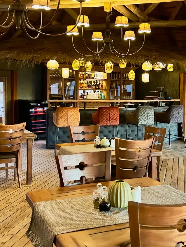 Open-plan lodge dining area with wooden furniture and bar overlooking landscape, Namib Outpost, Sossusvlei, Namibia