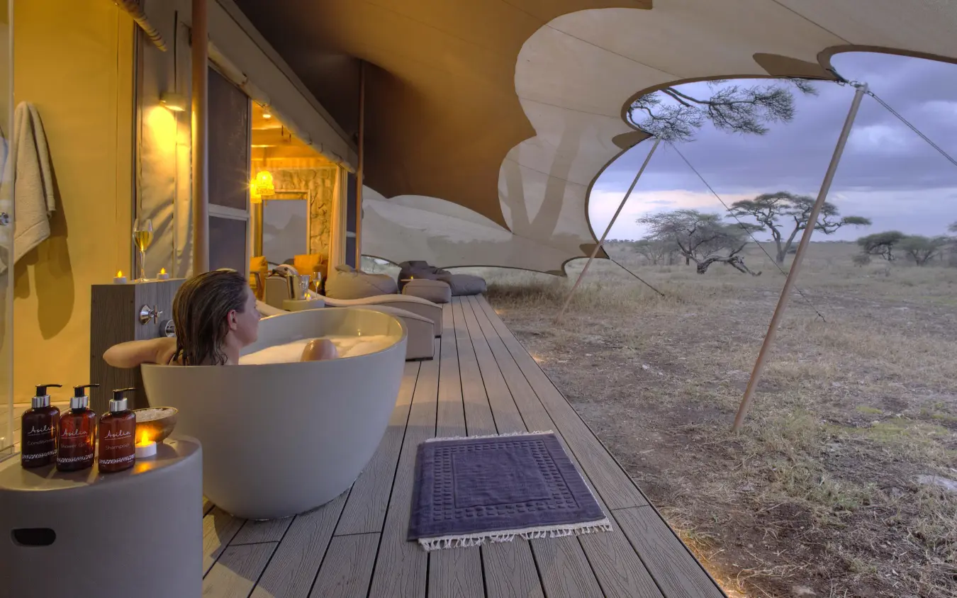 Guest soaking in outdoor bathtub on wooden deck at dusk, Namiri Plains, Serengeti National Park, Tanzania