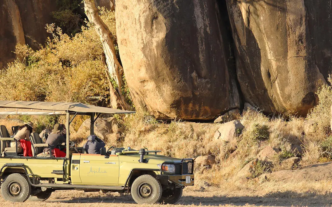 Safari vehicle with passengers near large rock formation, Namiri Plains, Serengeti National Park, Tanzania