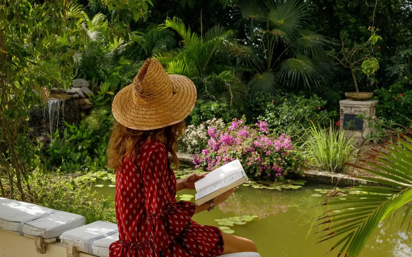 Woman reading by ornamental pond in lush tropical garden retreat, Nderit House, Kilifi, Kenya