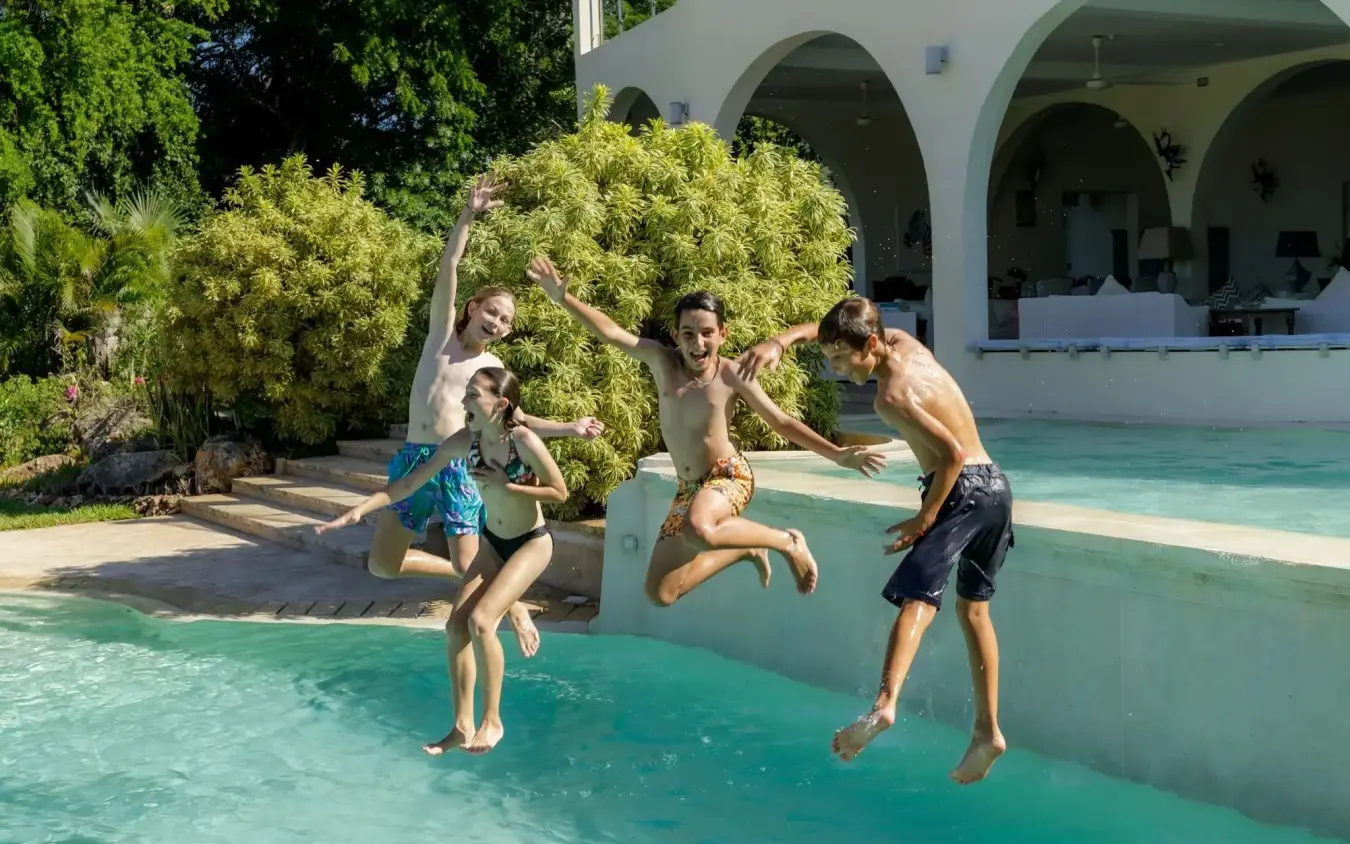 Family jumping into turquoise pool at beachfront villa with arched architecture, Nderit House, Kilifi, Kenya