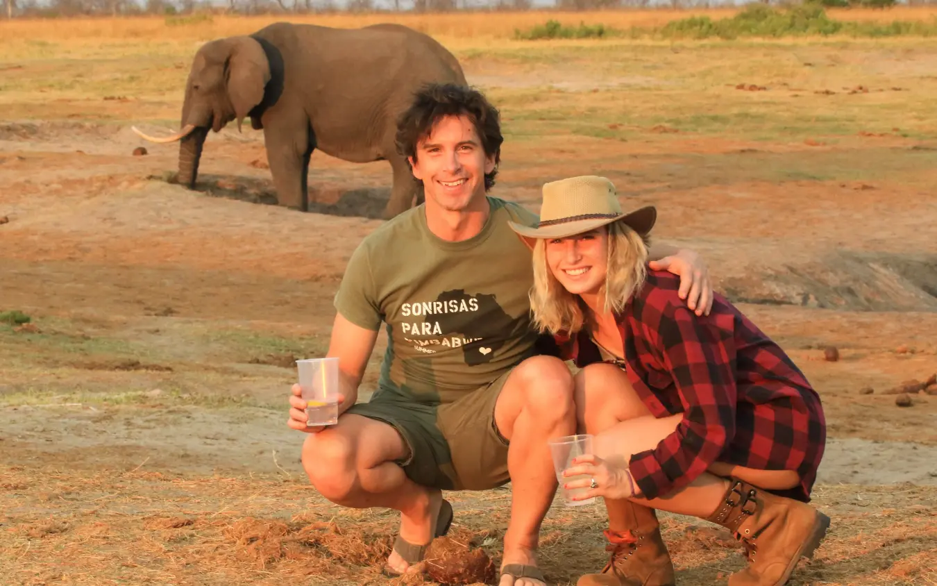 Couple posing with elephant in dusty wildlife sanctuary enclosure, Nehimba Lodge, Hwange National Park, Zimbabwe