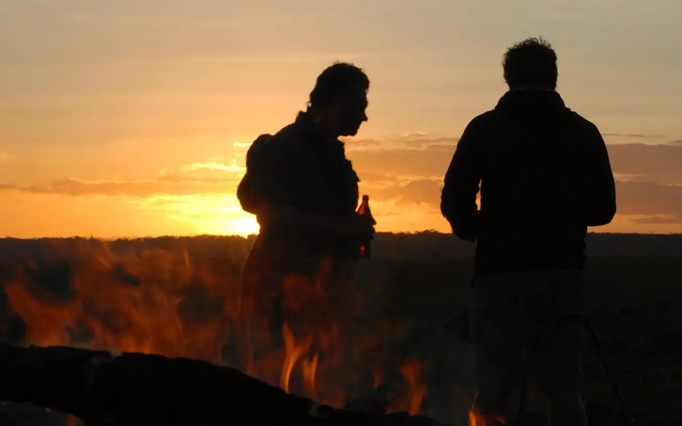 Two guests watching sunset fire performance at dusk, Ngare Serian, Maasai Mara, Kenya