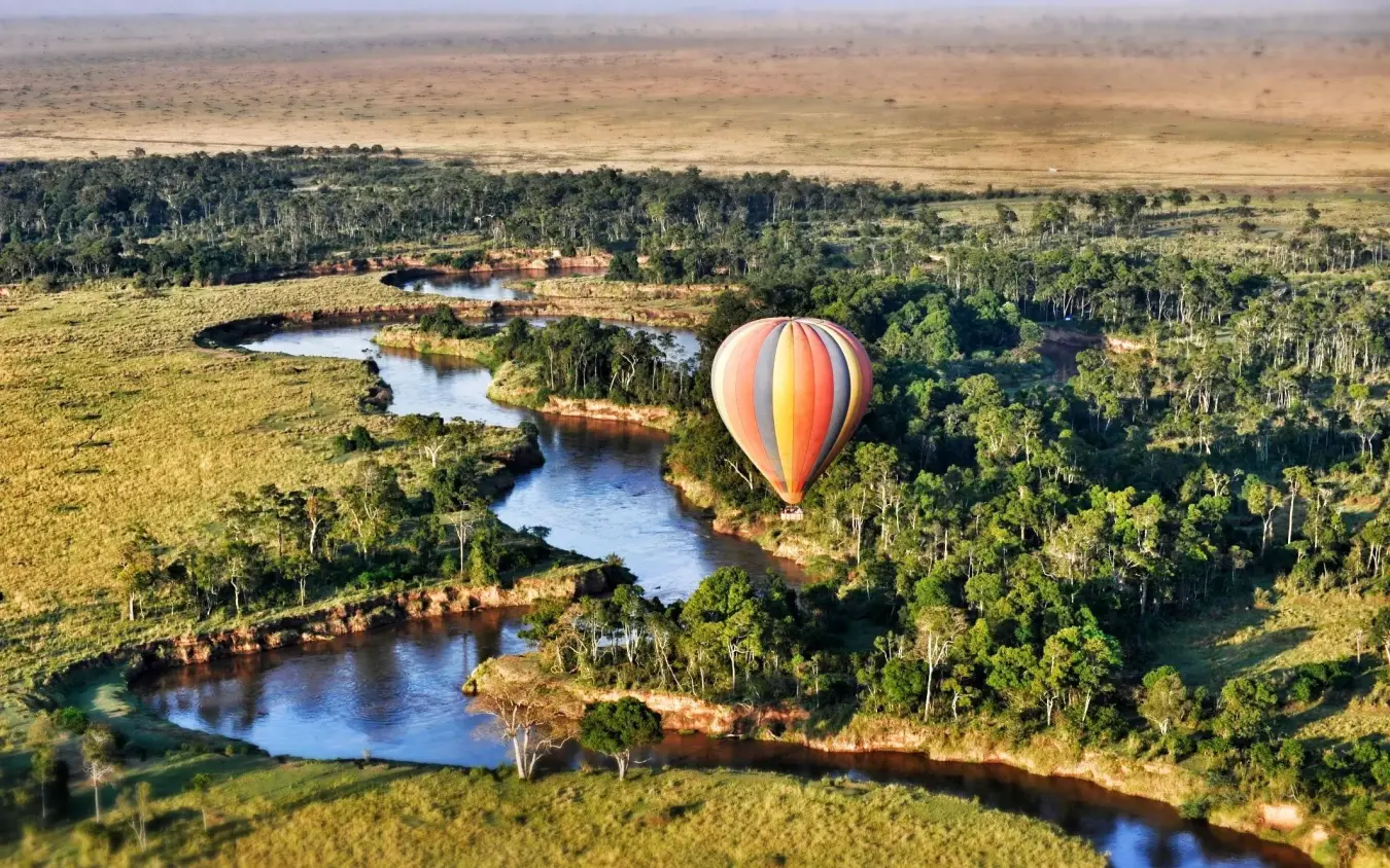 Hot air balloon floating over winding river and forest canopy, Ngare Serian, Maasai Mara, Kenya