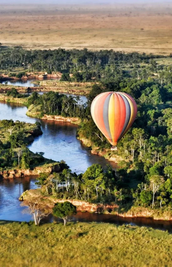 Hot air balloon floating over winding river and forest canopy, Ngare Serian, Maasai Mara, Kenya