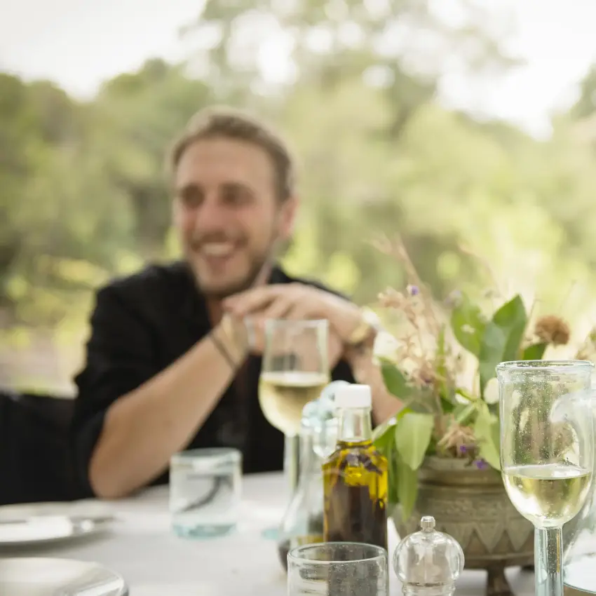 Man smiling at outdoor dining table with glassware, Ngare Serian, Maasai Mara, Kenya