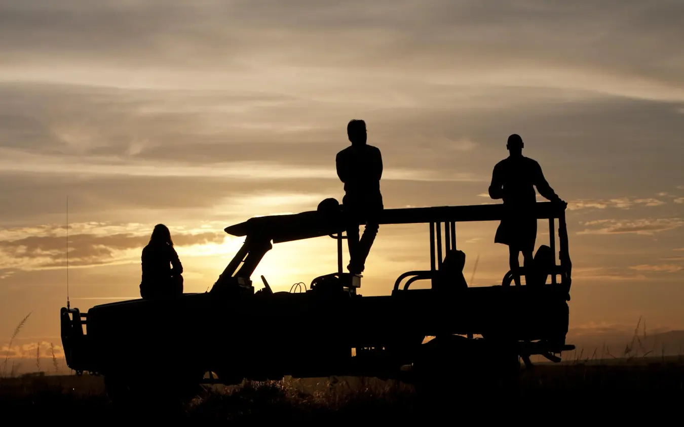Silhouetted guests on open safari vehicle at sunset, Ngare Serian, Maasai Mara, Kenya