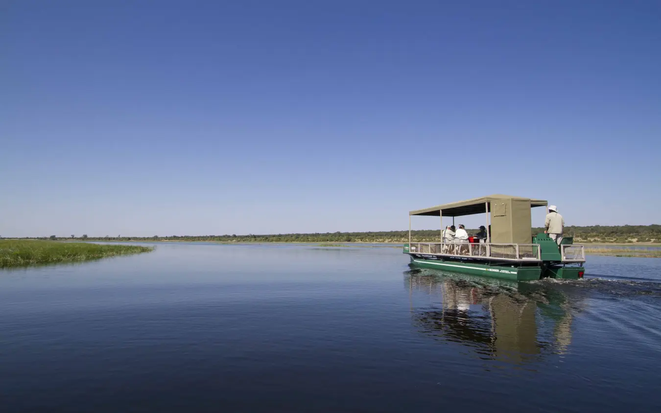 Motorboat with passengers cruising through wetland waterway at midday, Ngoma Safari Lodge, Chobe, Botswana