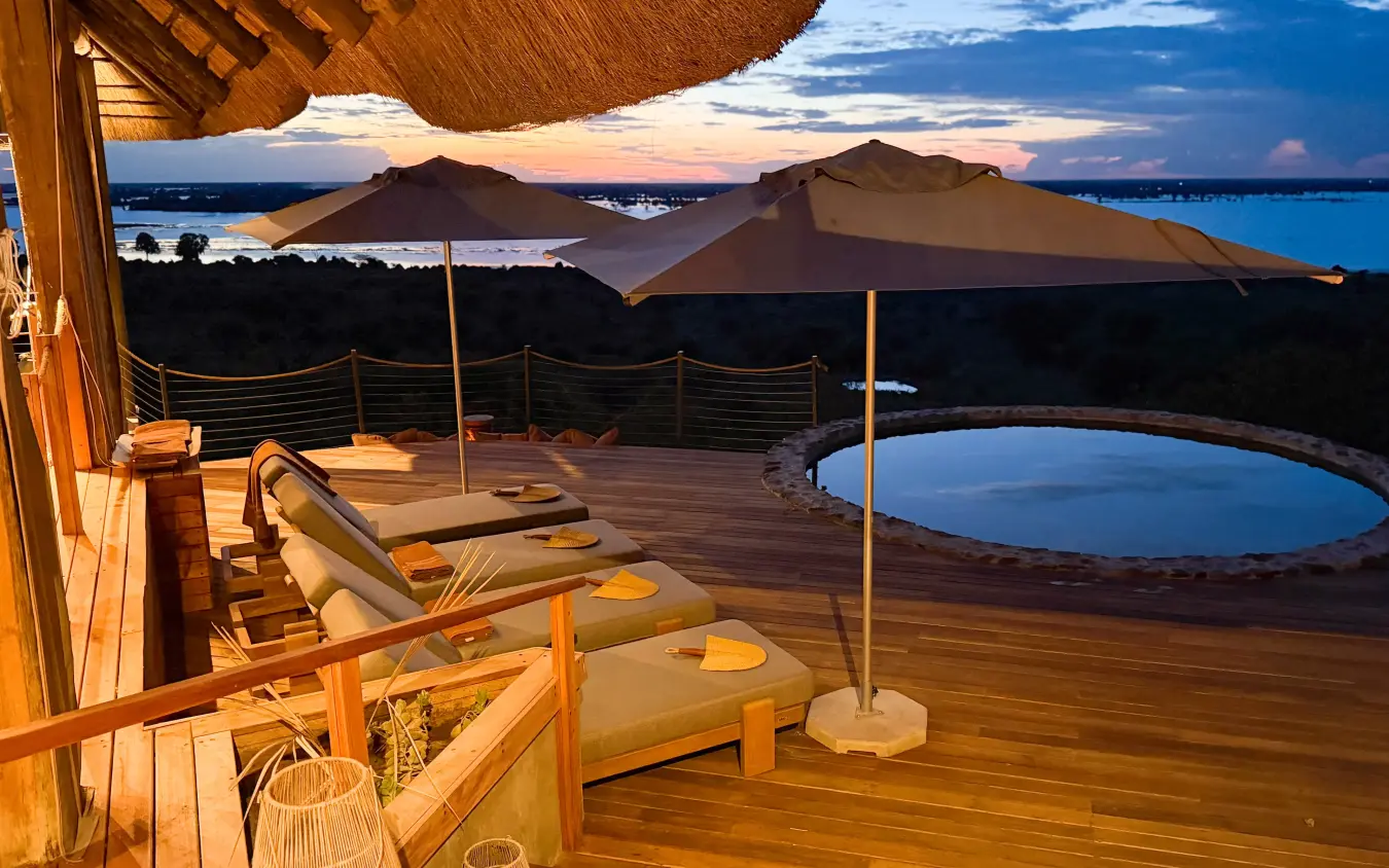 Wooden deck with loungers and umbrellas overlooking lake at dusk, Ngoma Safari Lodge, Chobe, Botswana