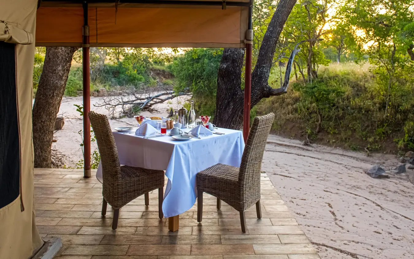 Intimate dining setup on wooden deck overlooking riverbed, Nimali Tarangire, Tarangire National Park, Tanzania