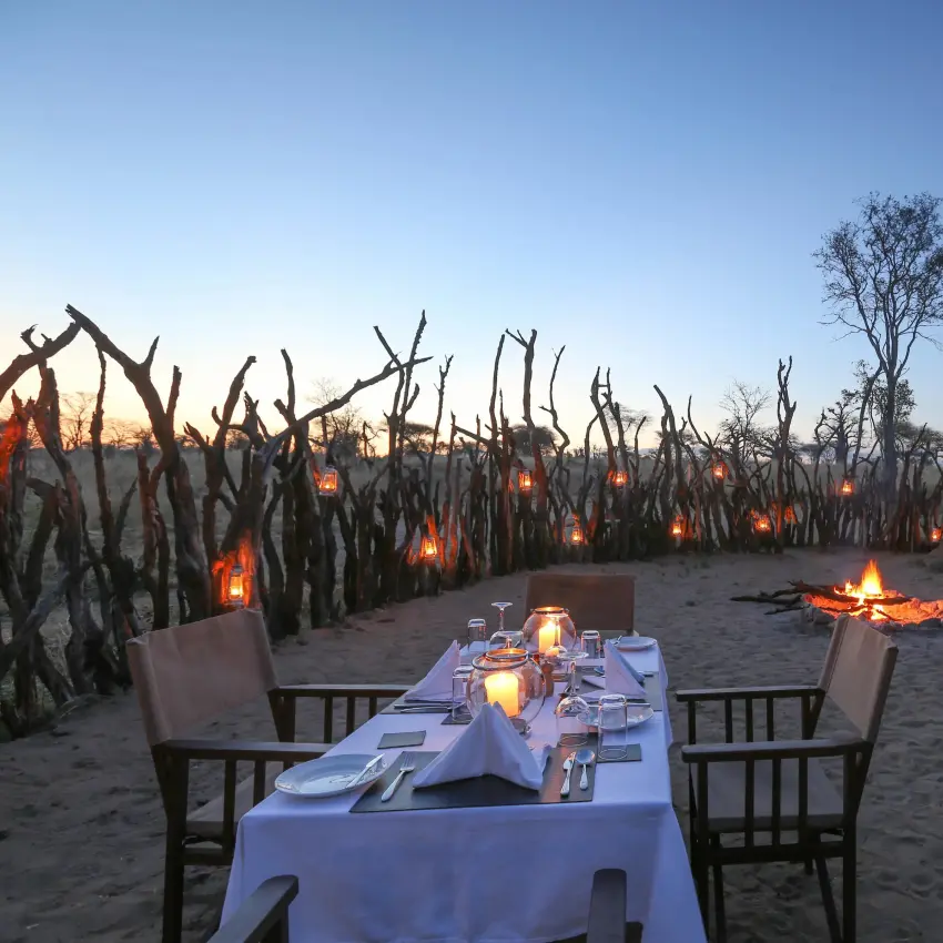 Outdoor dinner table set on sandy ground at dusk, Nimali Tarangire, Tarangire National Park, Tanzania