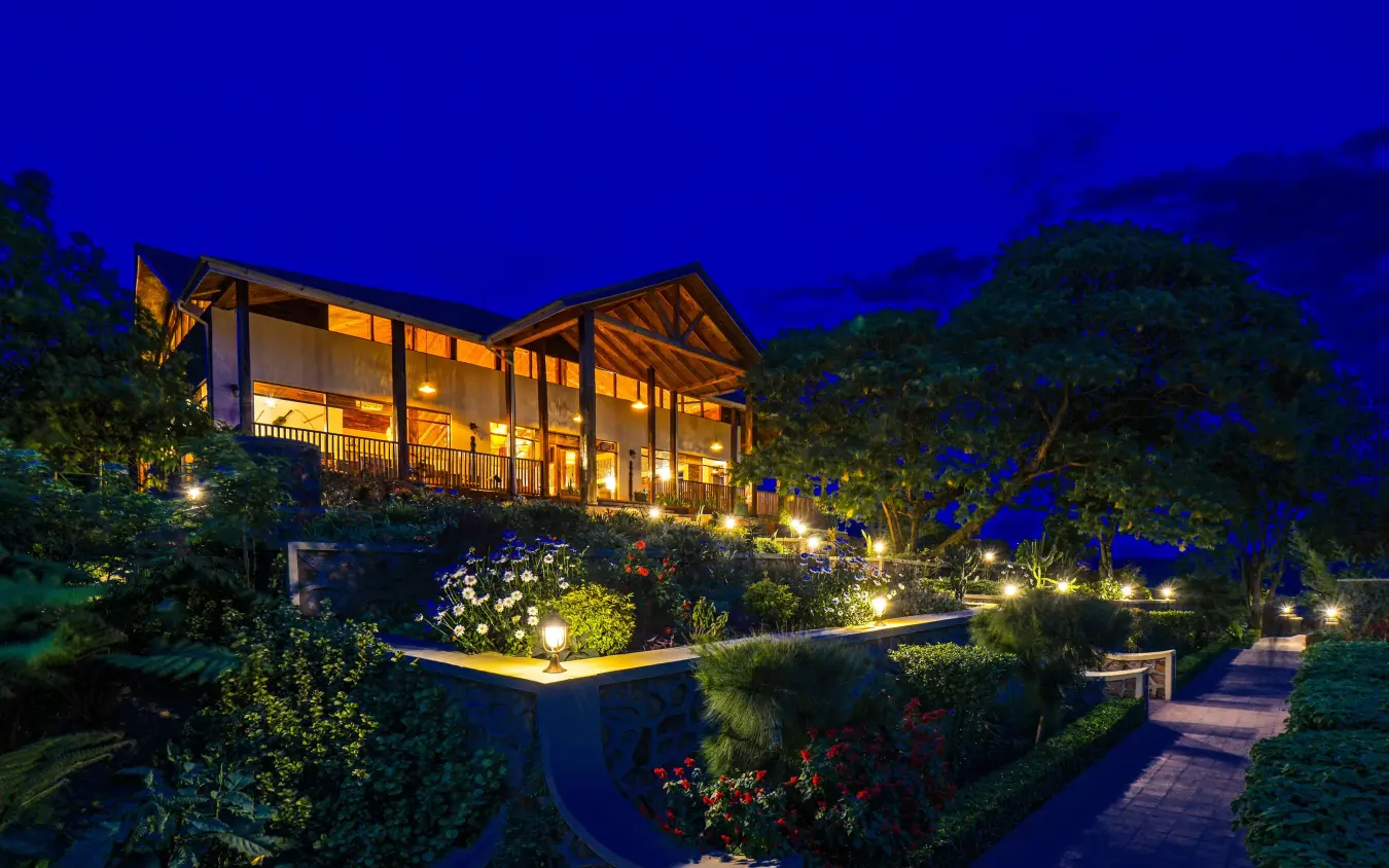 Illuminated lodge building at dusk surrounded by landscaped gardens, Nkuringo Gorilla Lodge, Bwindi Impenetrable Forest, Uganda