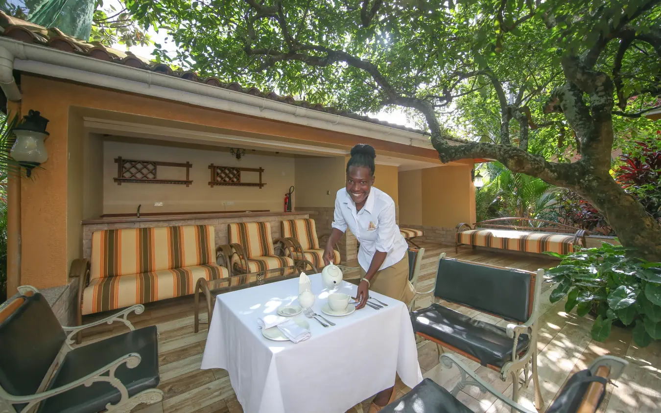 Staff member setting table on covered patio with striped furniture, No.5 Boutique Hotel, Entebbe and Kampala, Uganda