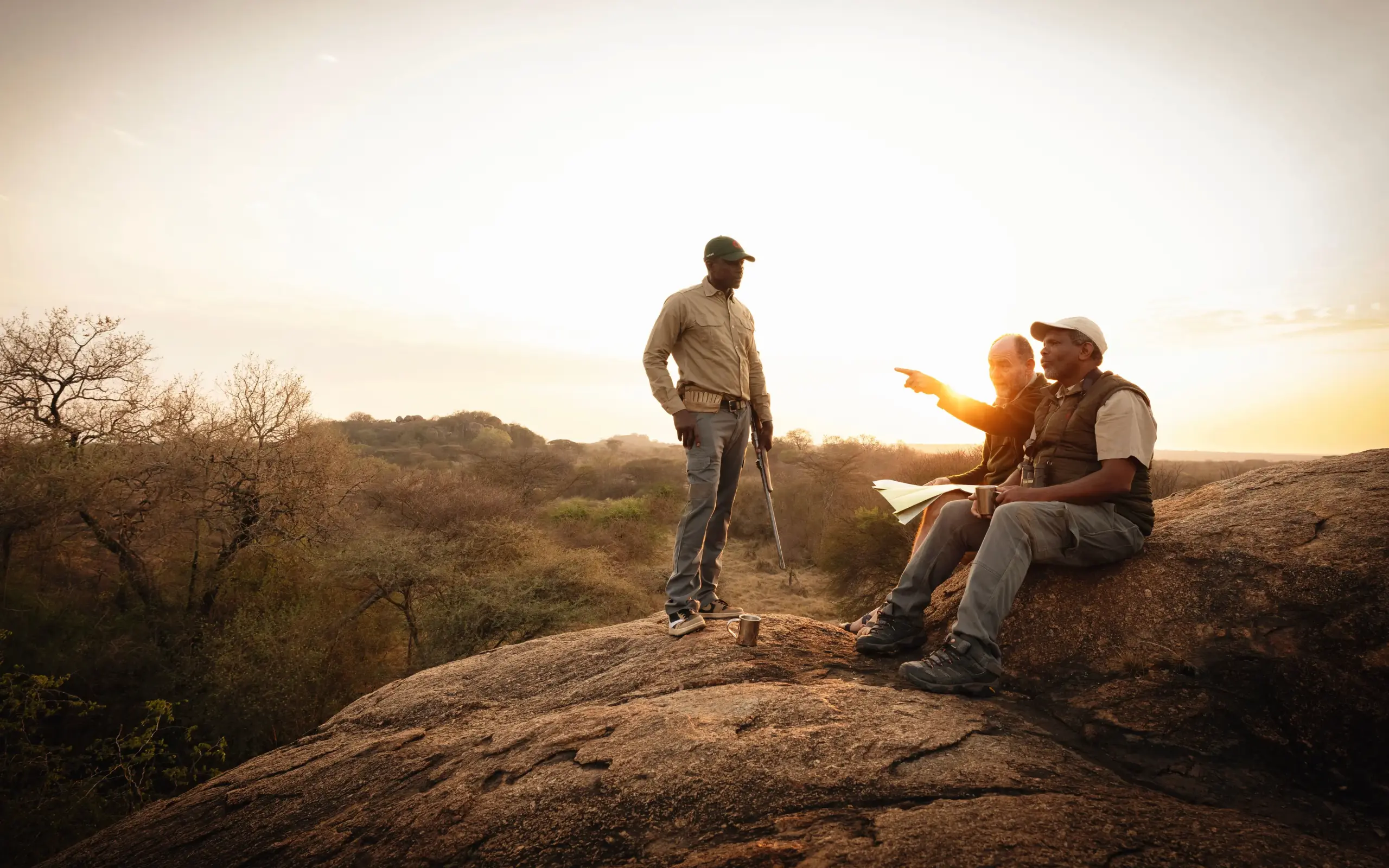 Guides pointing across savanna landscape at sunset, Tanzania