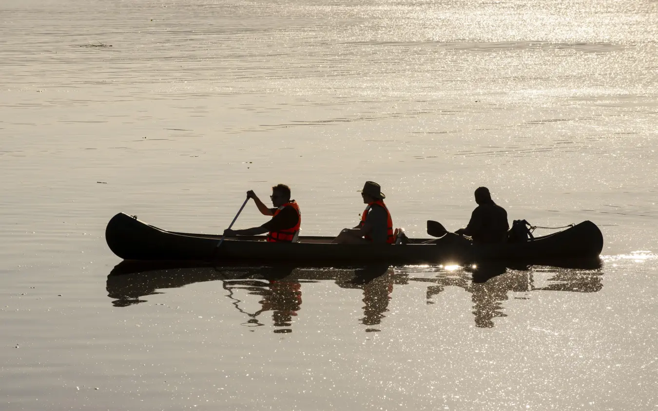 Silhouetted guests paddling canoe on calm water at sunrise, Nyamatusi Camp, Mana Pools, Zimbabwe
