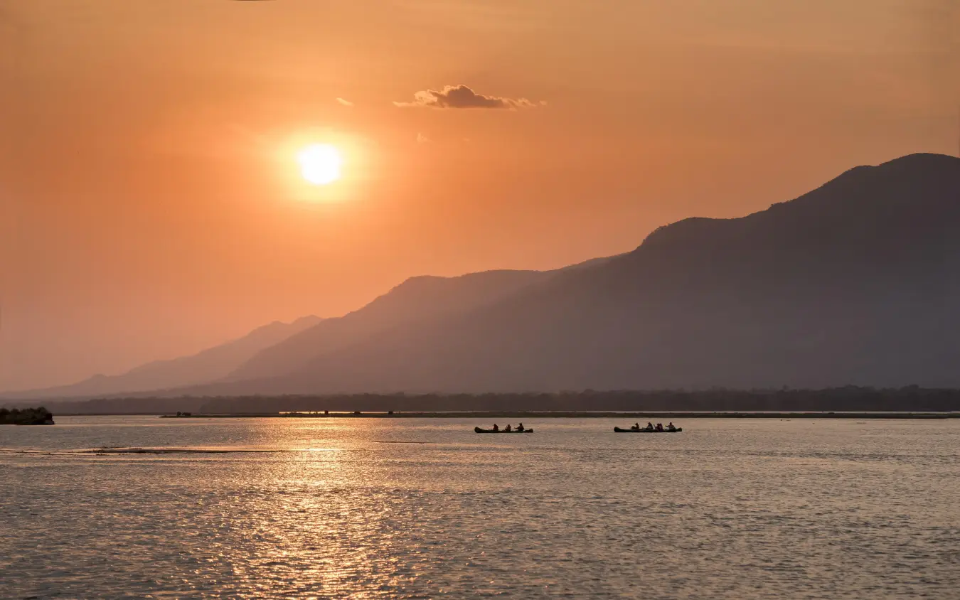 Sunset over water with mountains and small boats, Nyamatusi Camp, Mana Pools, Zimbabwe