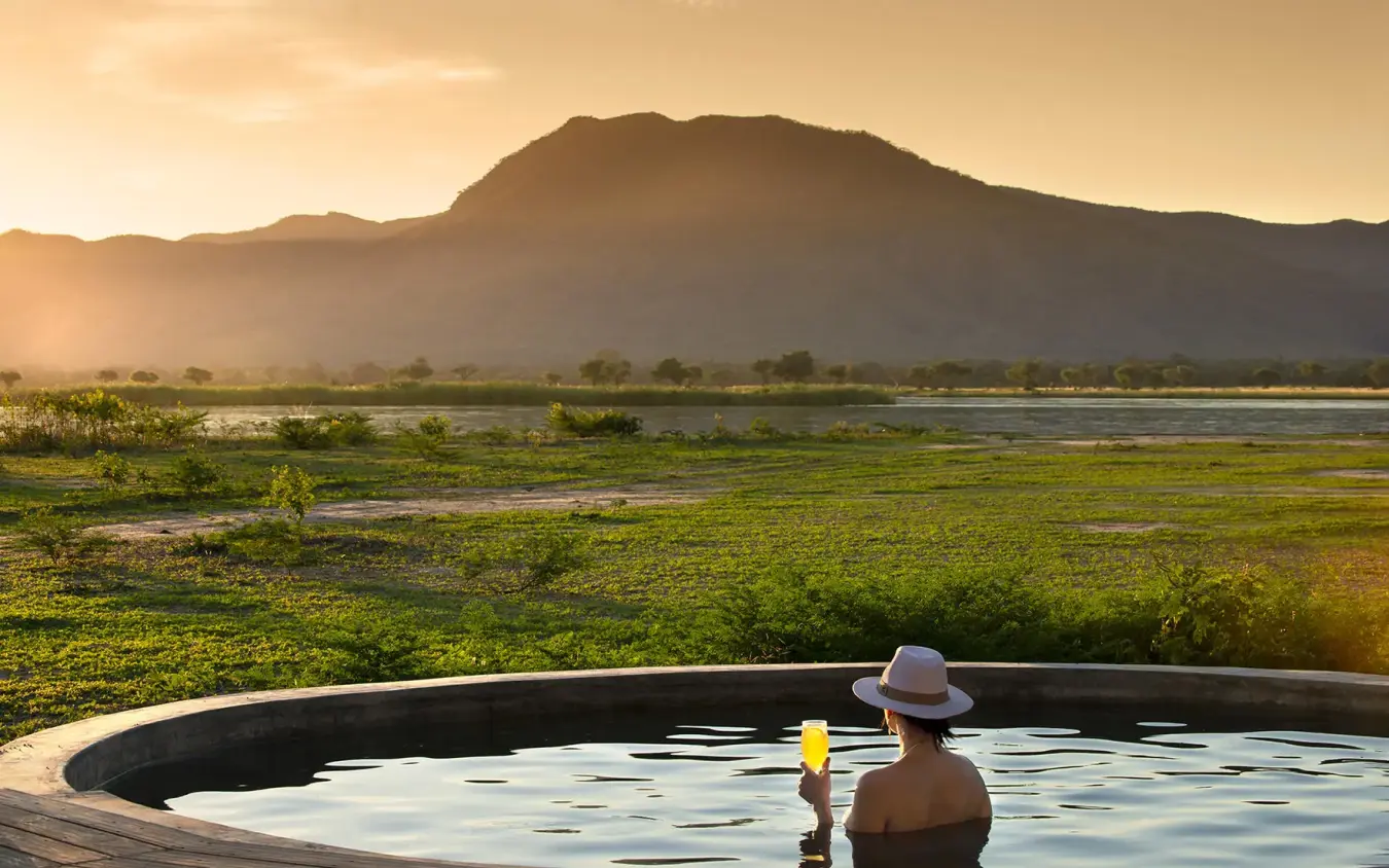 Guest relaxing in infinity pool overlooking river valley, Nyamatusi Camp, Mana Pools, Zimbabwe