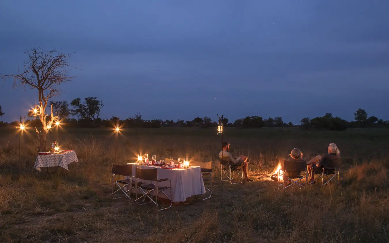 Guests gathered around campfires under twilight sky, Kweene Trails, The Okavango Delta, Botswana