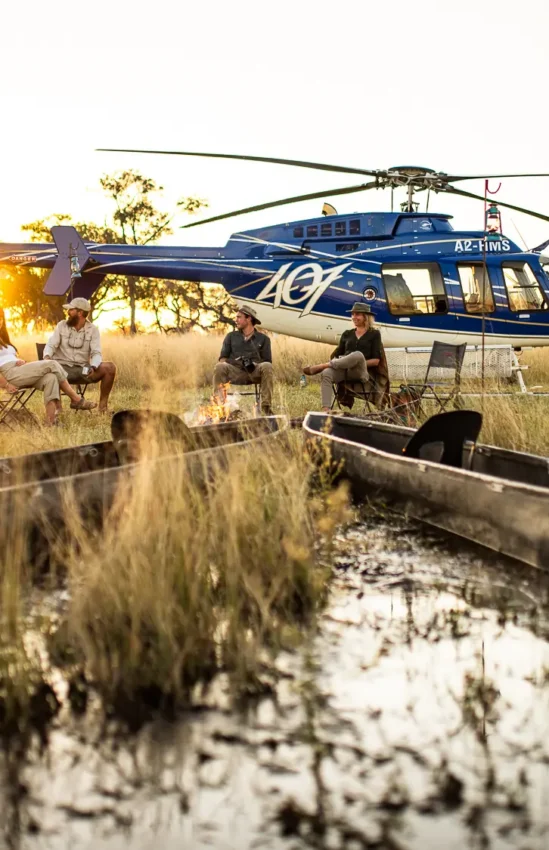 Helicopter arrival at remote waterway with boats and staff, Kweene Trails, The Okavango Delta, Botswana