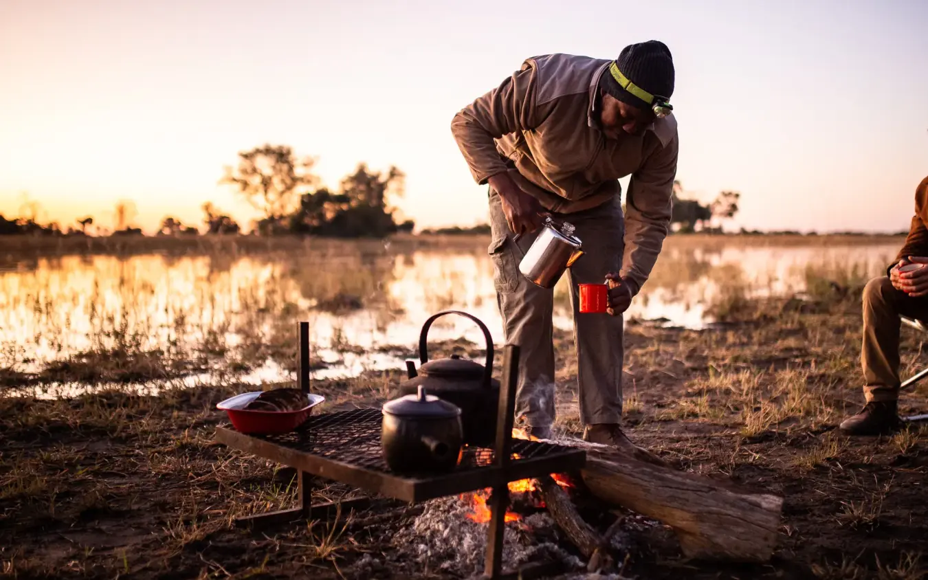Guide preparing tea at campfire during safari expedition, Kweene Trails, The Okavango Delta, Botswana