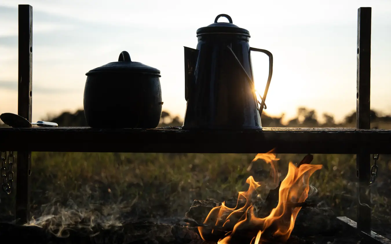 Cooking pots heating over open campfire at sunset, Kweene Trails, The Okavango Delta, Botswana
