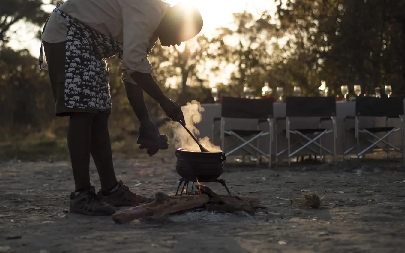 Person tending campfire at sunset during outdoor gathering