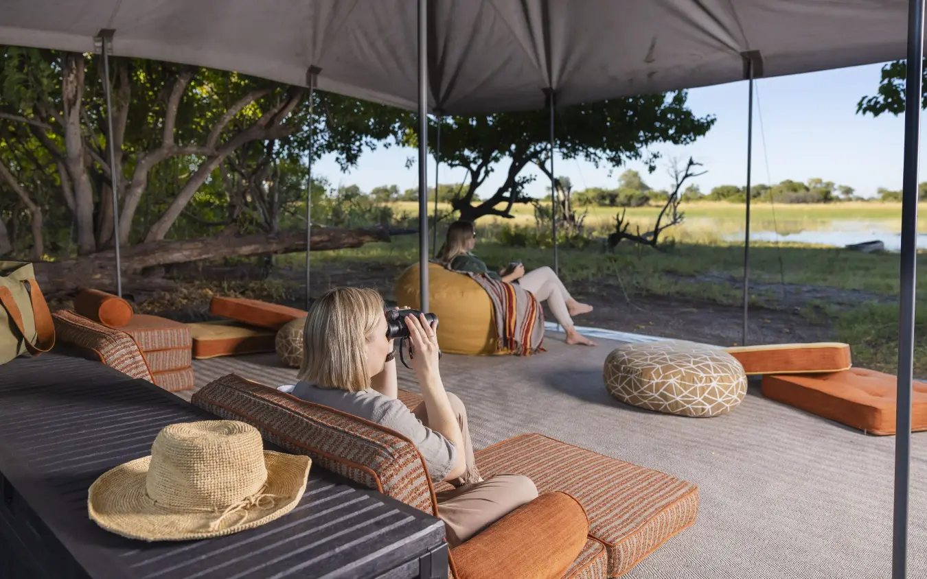 Guests relaxing on shaded deck overlooking waterhole landscape, Kweene Trails, The Okavango Delta, Botswana