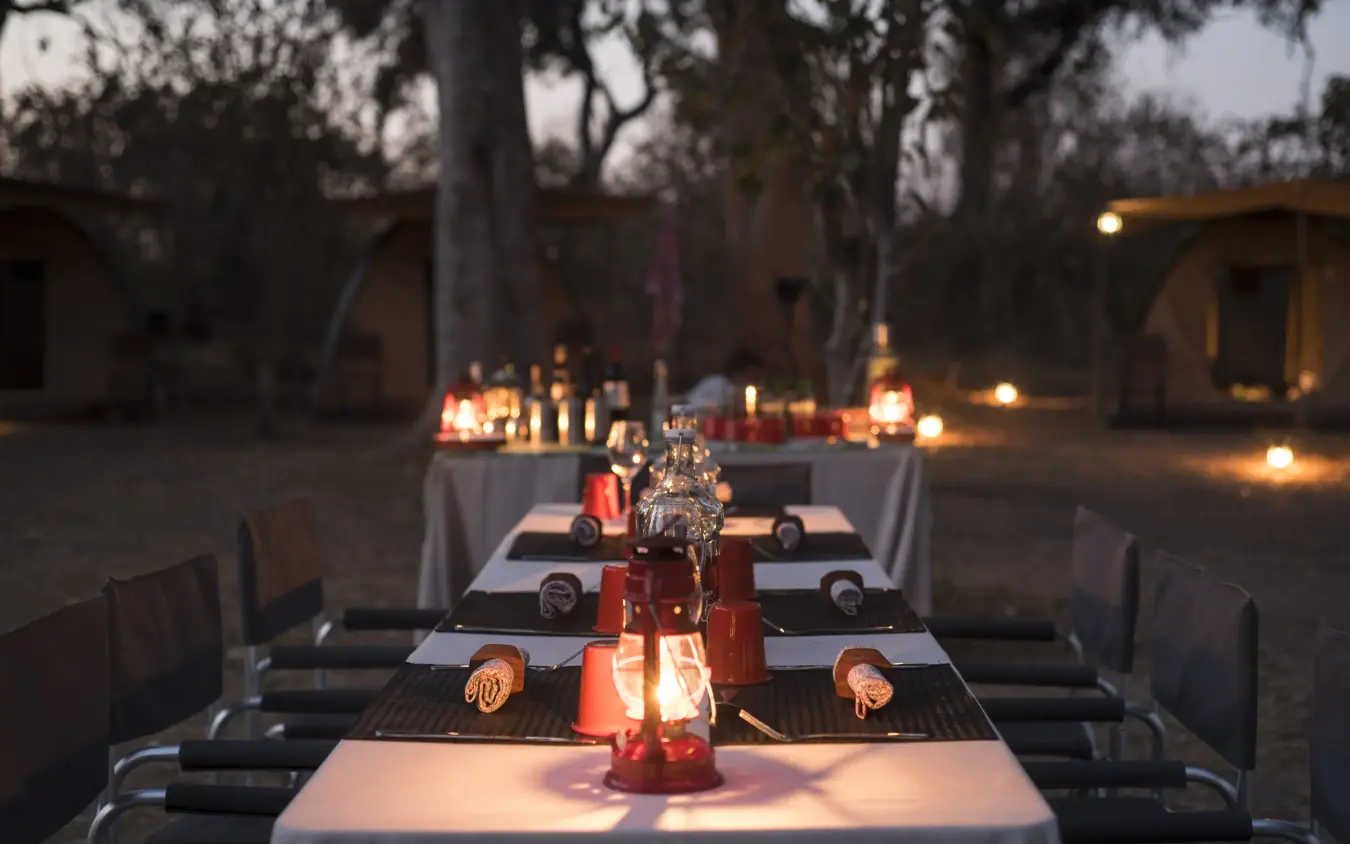 Evening outdoor dining setup with candlelit tables under trees, Kweene Trails, The Okavango Delta, Botswana
